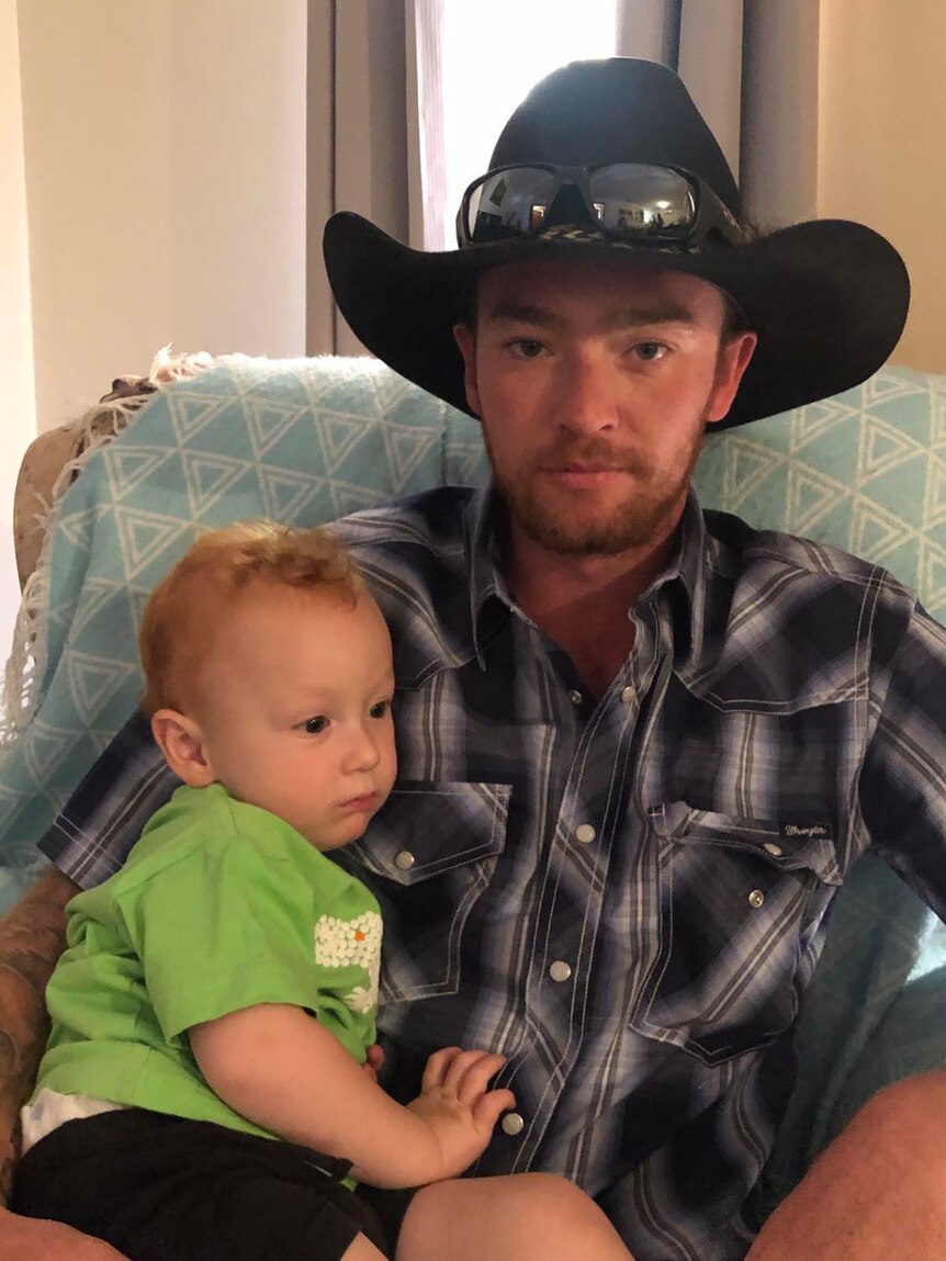 A man in an Akubra cuddles his young son, who is in a green top.