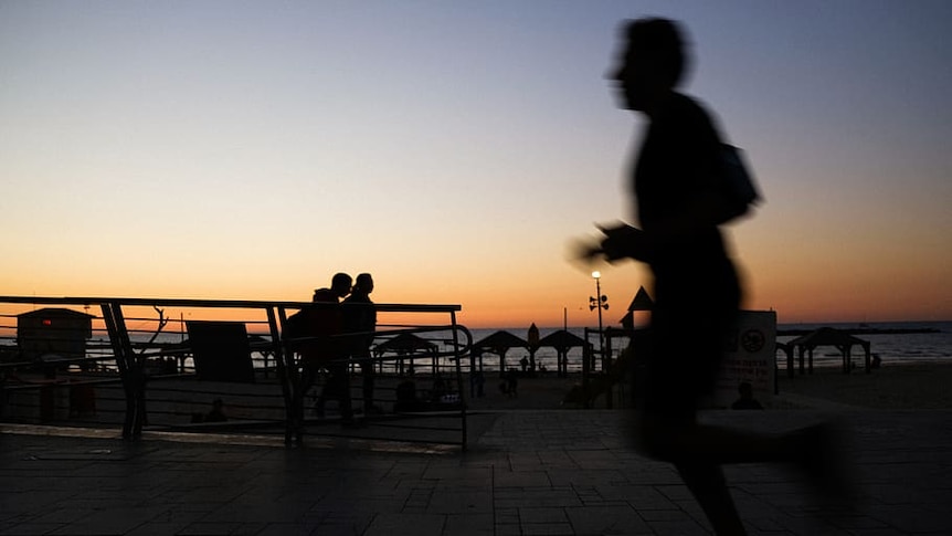 Silhouette of a man jogging next to a beach.