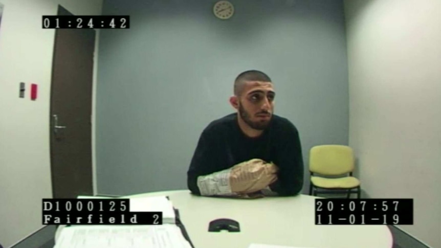 a man with paper bags around his hands being interviewed by police in a room