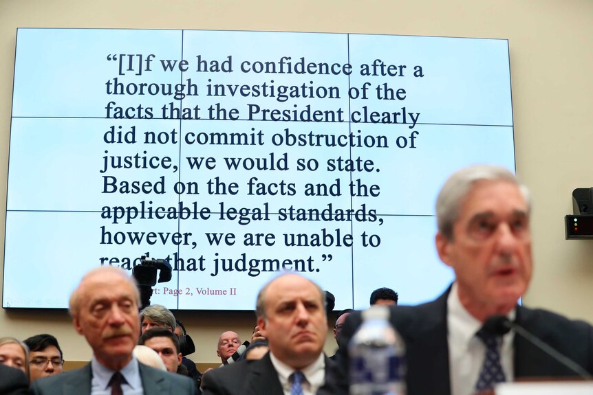 A large screen with a quote from the Mueller report appears before a group of people at a congressional judiciary committee.