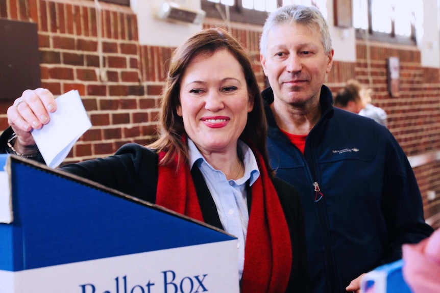 Tania Lawrence casts her Darling Range vote in a blue ballot box with a man standing behind her looking on.