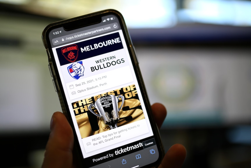 A smartphone displaying the website for purchasing tickets to the 2021 AFL grand final on screen is a premiership cup