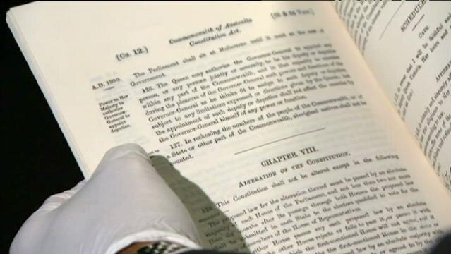 Gloved hands hold open pages of Australian Constitution