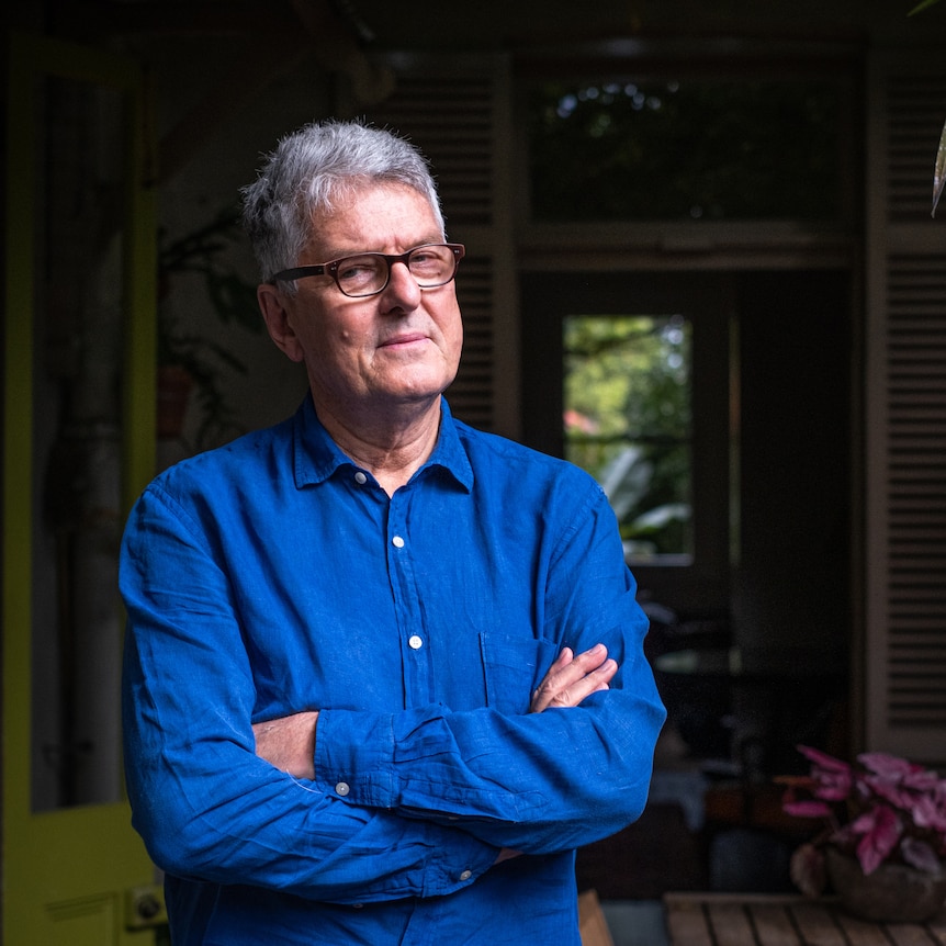 David Marr stands just outside a house, his arms crossed.