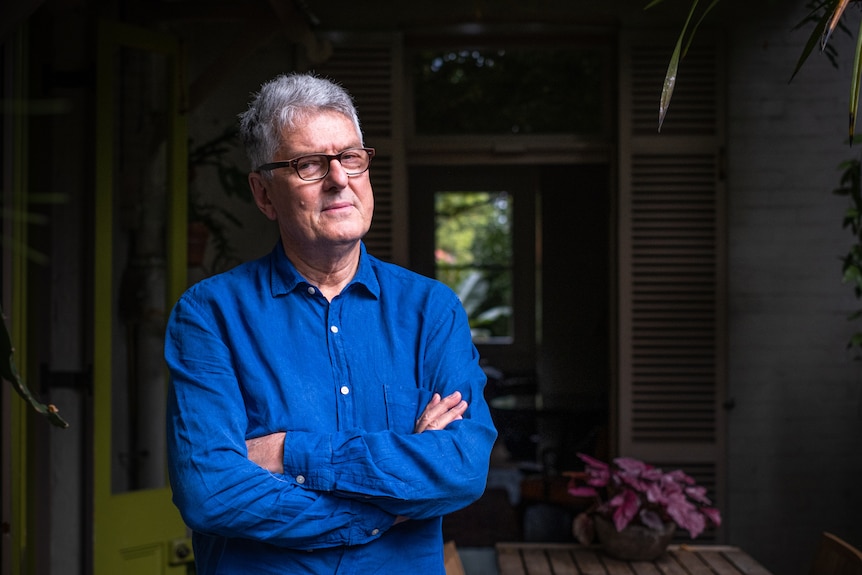 David Marr stands just outside a house, his arms crossed.