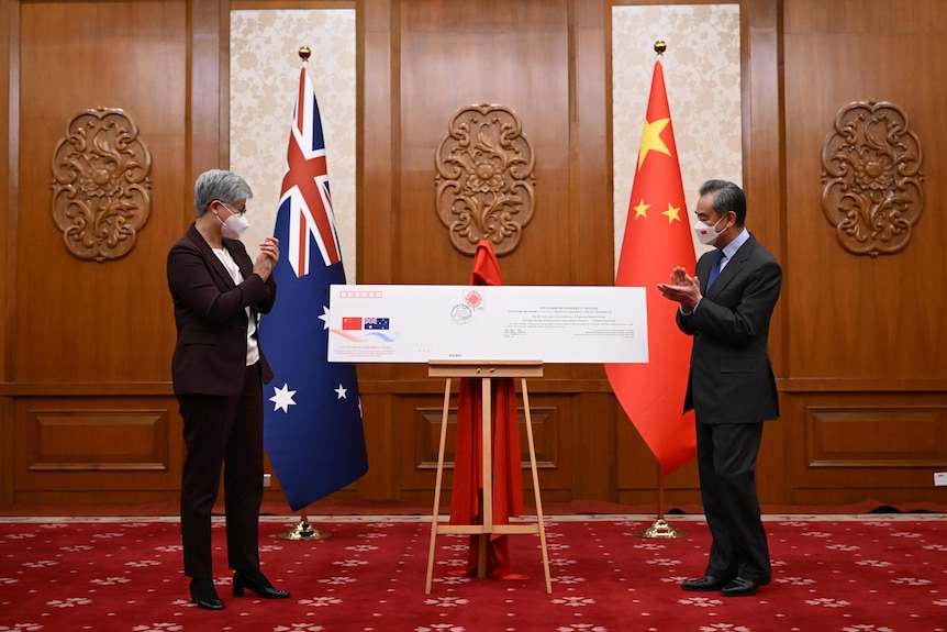 Wang Yi and Penny Wong stand next to a large envelope with China Australia flags in the background. 