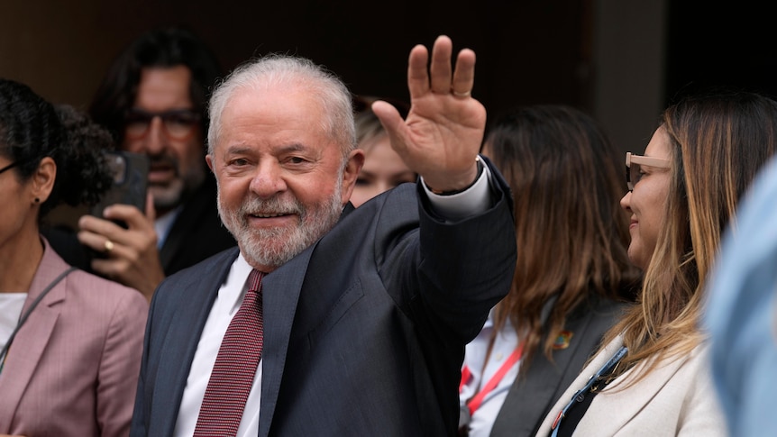 Brazilian president-elect Luiz Inacio Lula da Silva in a suit waves toward the camera as he walks in a crowd of people 