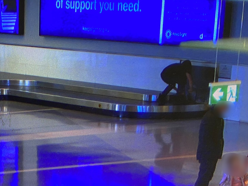 CCTV image of a young person in dark clothing on an airport baggage carousel.