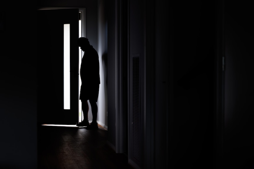 A silhouette of a man standing at his front door.