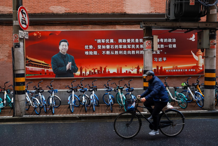 On the street of Beijing, a cyclist rides past a banner that promotes Chinese president Xi Jinping's speech. 