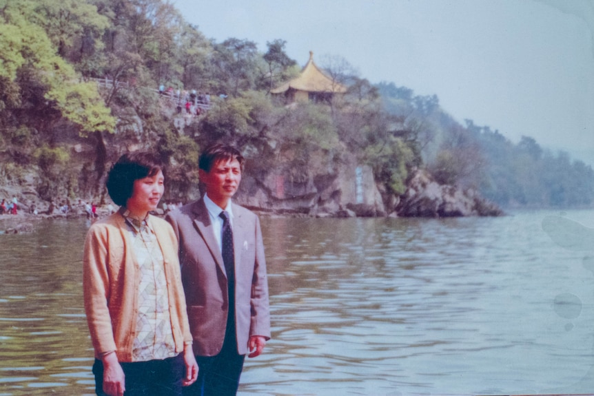 A young Chinese couple pose by a waterway.