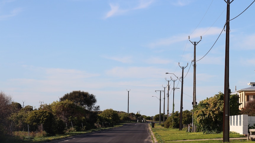 A clear sky with powerlines on the right, a road with some house fronts