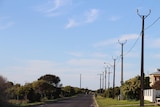 A clear sky with powerlines on the right, a road with some house fronts