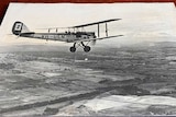 Biplane in flight pictured in a black and white photo.