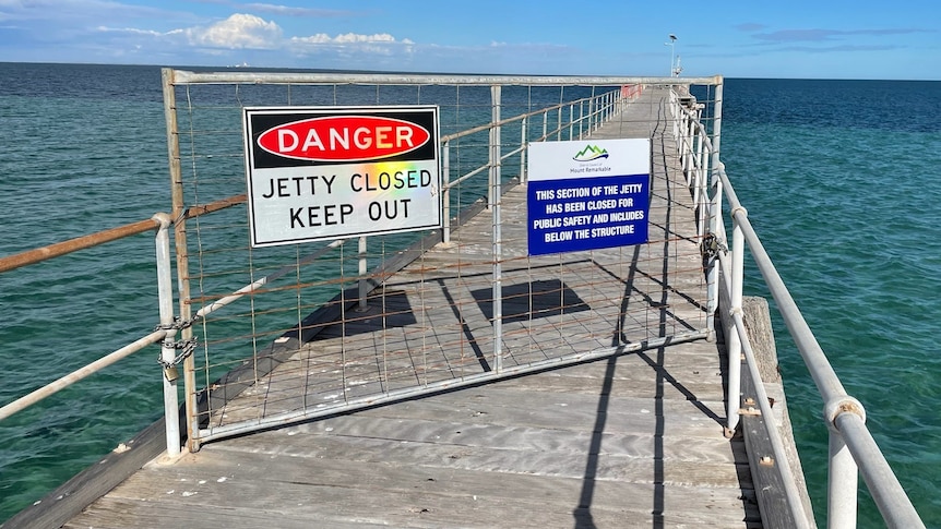 A metal fence with 'Danger' on it sits on a timber jetty against a turquoise ocean.