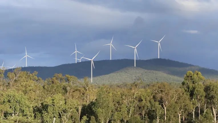 Wind turbines on top of a ridge, with trees below