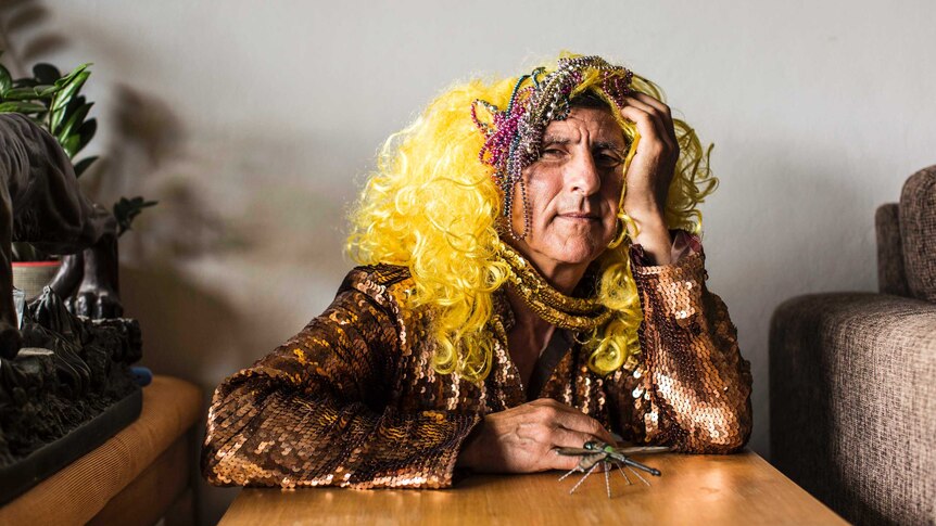 Kim Gotlieb wearing sequinned dress and wig with beads on head. Small glass dragonfly sits beside him.