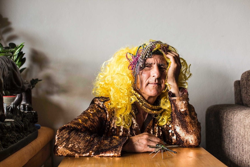 Kim Gotlieb wearing sequinned dress and wig with beads on head. Small glass dragonfly sits beside him.