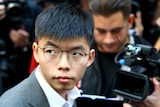 Joshua Wong looks over his shoulder with people with cameras pointing at him in the background.