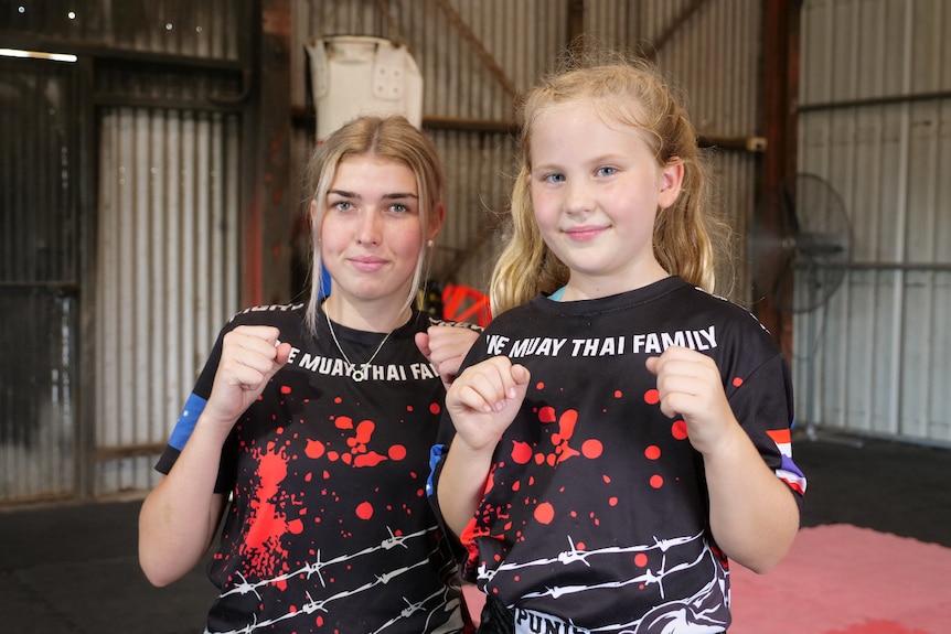 A young girl and a teenager are side-by-side with their hands raised in fists. 