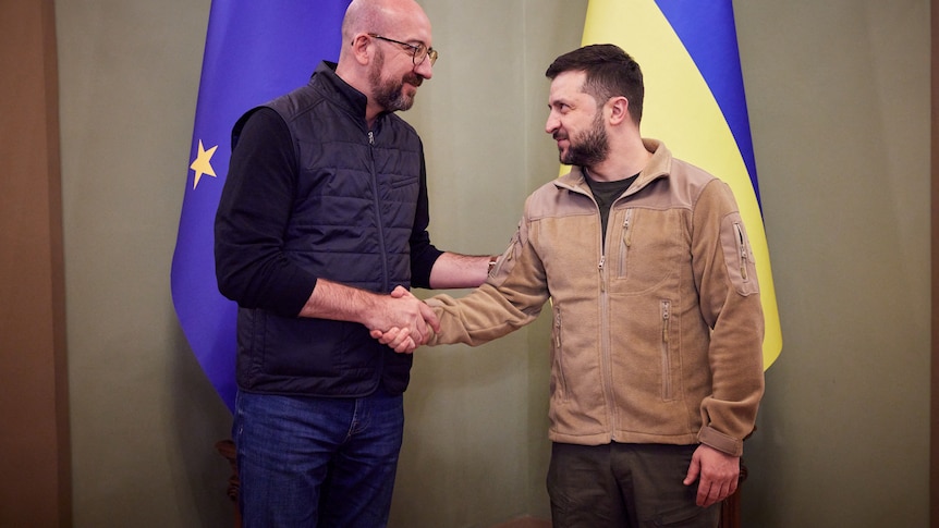 Two men shake hands infront of the European Union flag and the Ukrainian flag