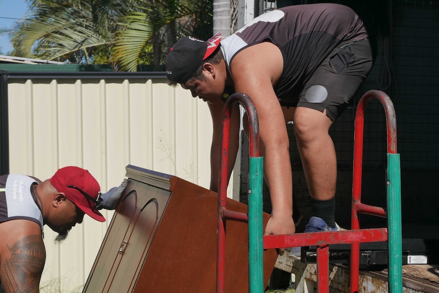 Eto Saursoo and Nathan Siaki lift a wardrobe into the back of a moving truck.
