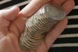 The small hand of a woman rests on a lap, holding a stack of 20 50-cent pieces.