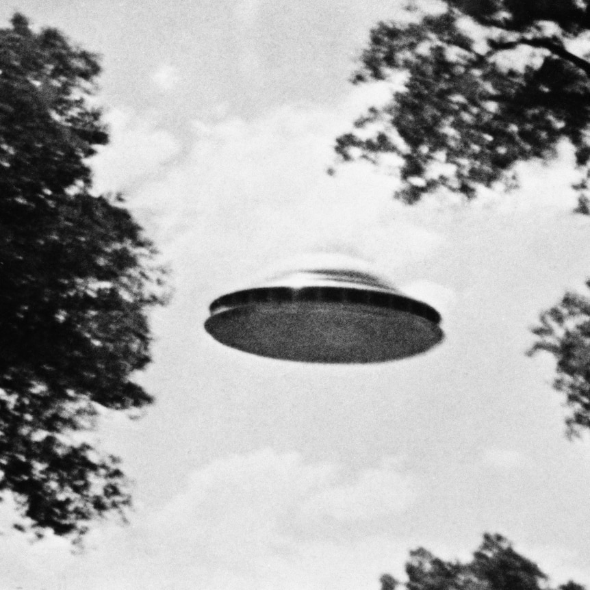 A black and white photo of a metallic disk flying through the sky