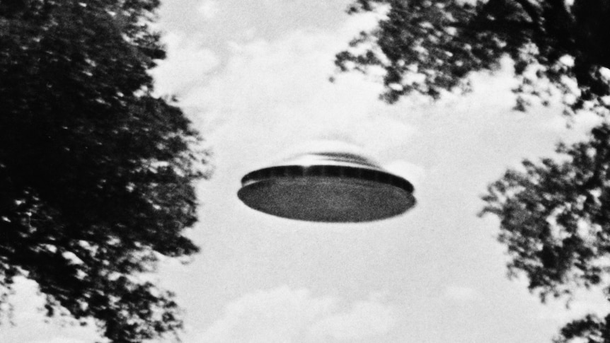 A black and white photo of a metallic disk flying through the sky
