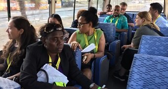 A bus carries members of the local PNG and international media. All are wearing lanyards.