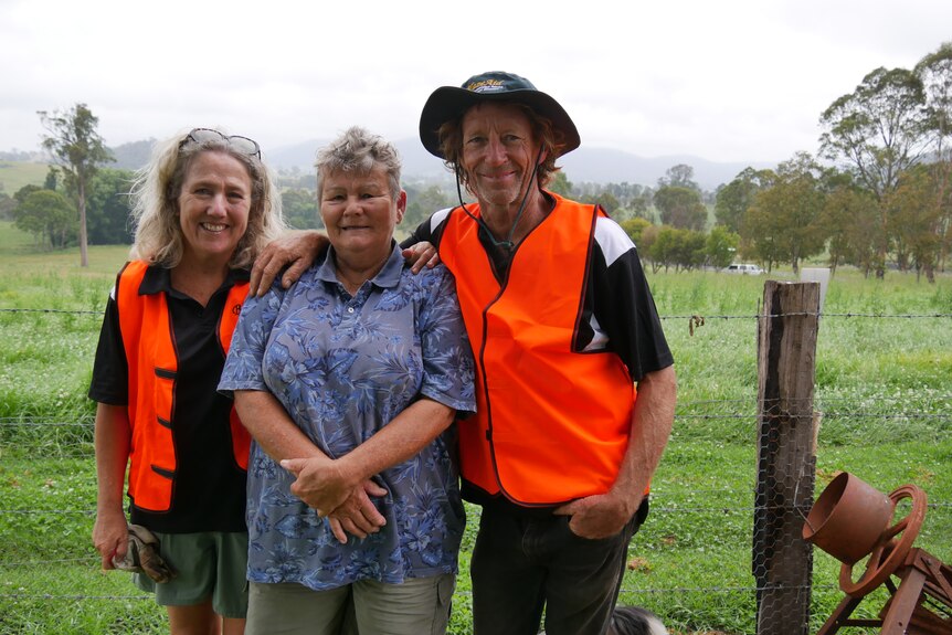 Two people in orange vests with a woman in a blue dress in a paddock