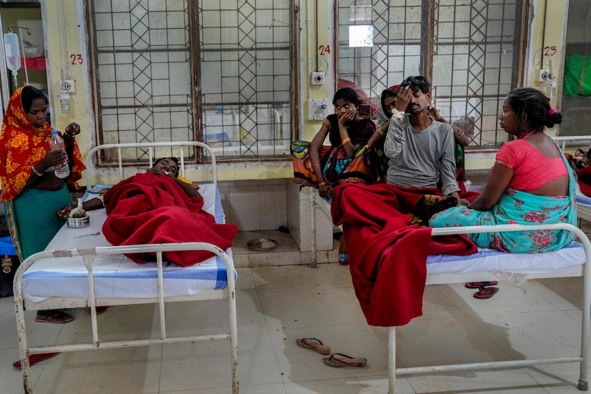 Sonu Devandan lies on a bed next a group of people sitting on bed inside the hospital in Ambikapur
