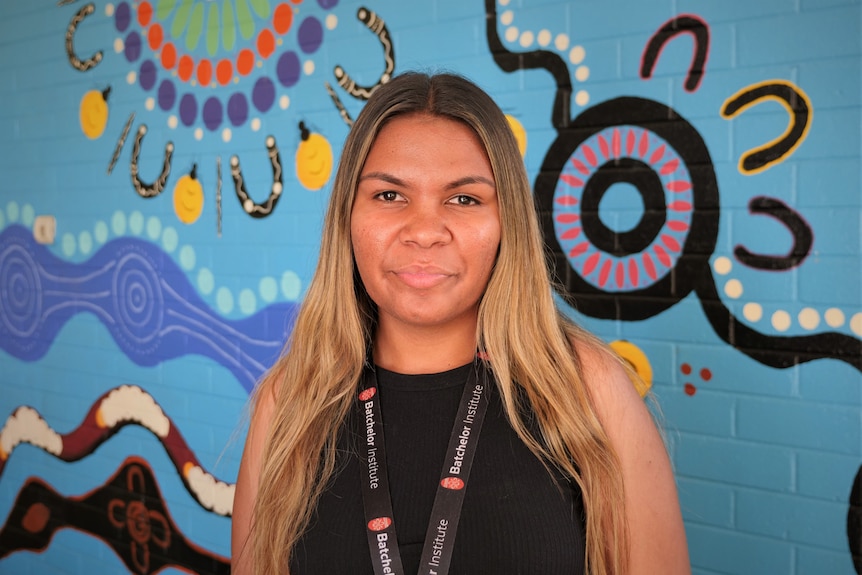 An Indigenous woman in front of a colourful wall.