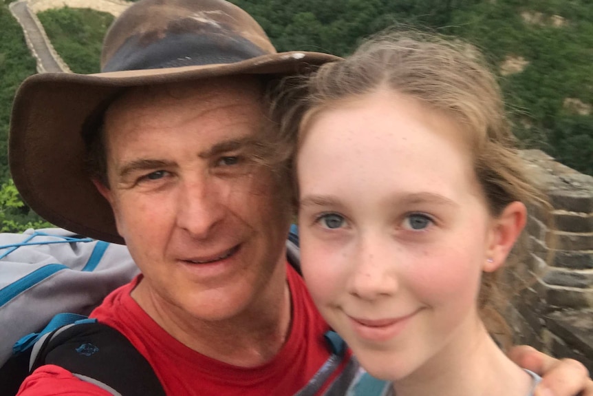 A man in a hat and a girl stand on the Great Wall in China with a green hill behind them