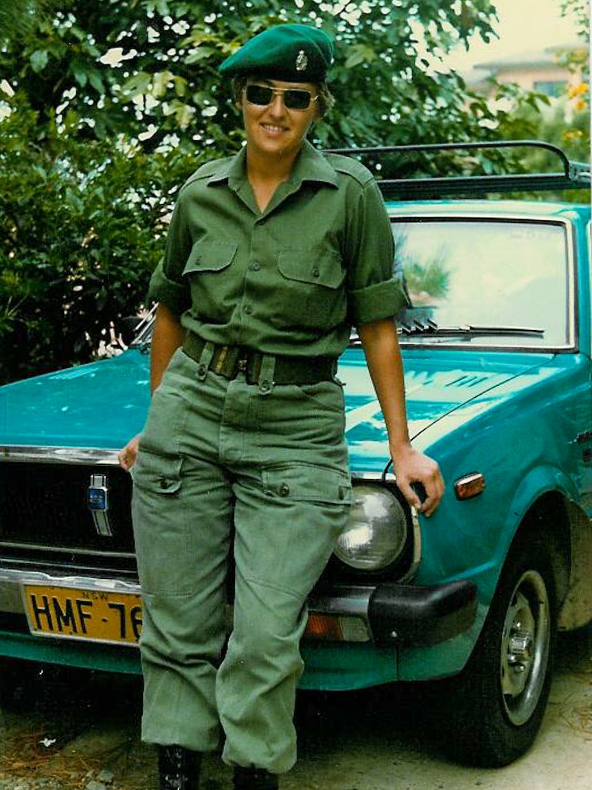 A woman dressed in army uniform in front of a sedan car.