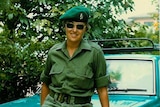 A woman dressed in army uniform in front of a sedan car.