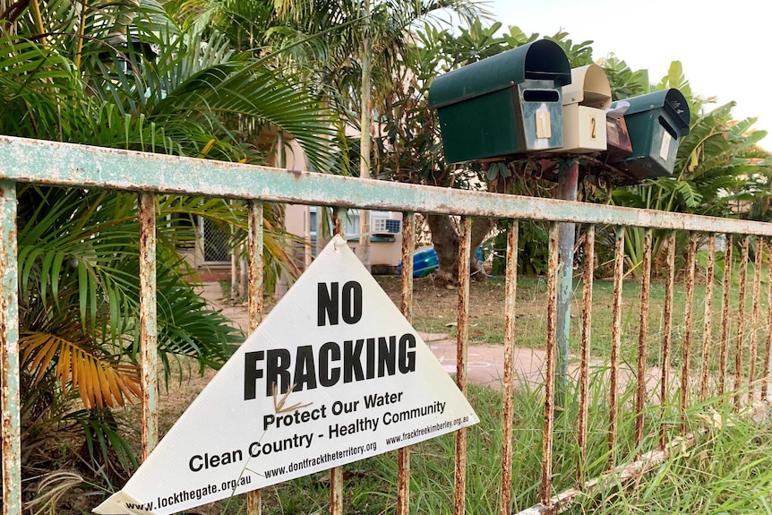 A sign hanging on a fence reading 'No Fracking, Protect Our Water, Clean Country - Healthy Community', next to four letterboxes