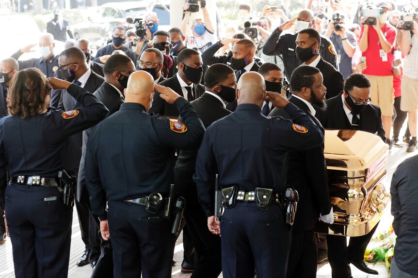 A row of police officers salute as George Floyd's body arrives before his funeral service at the Fountain of Praise Church.