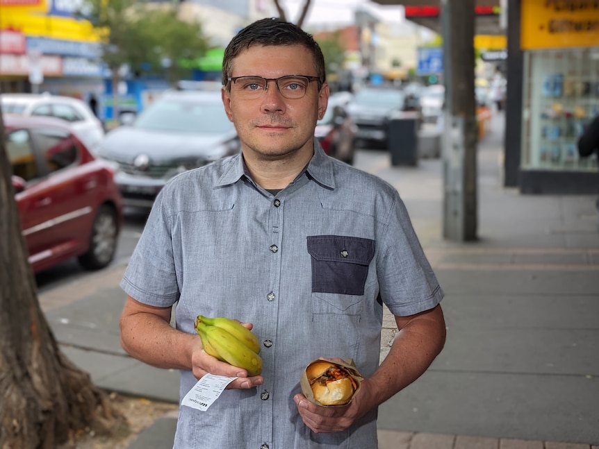 A man holding a bunch of bananas and a banh mi.
