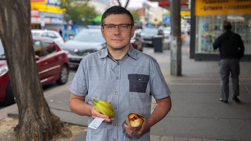 A man holding a bunch of bananas and a banh mi.