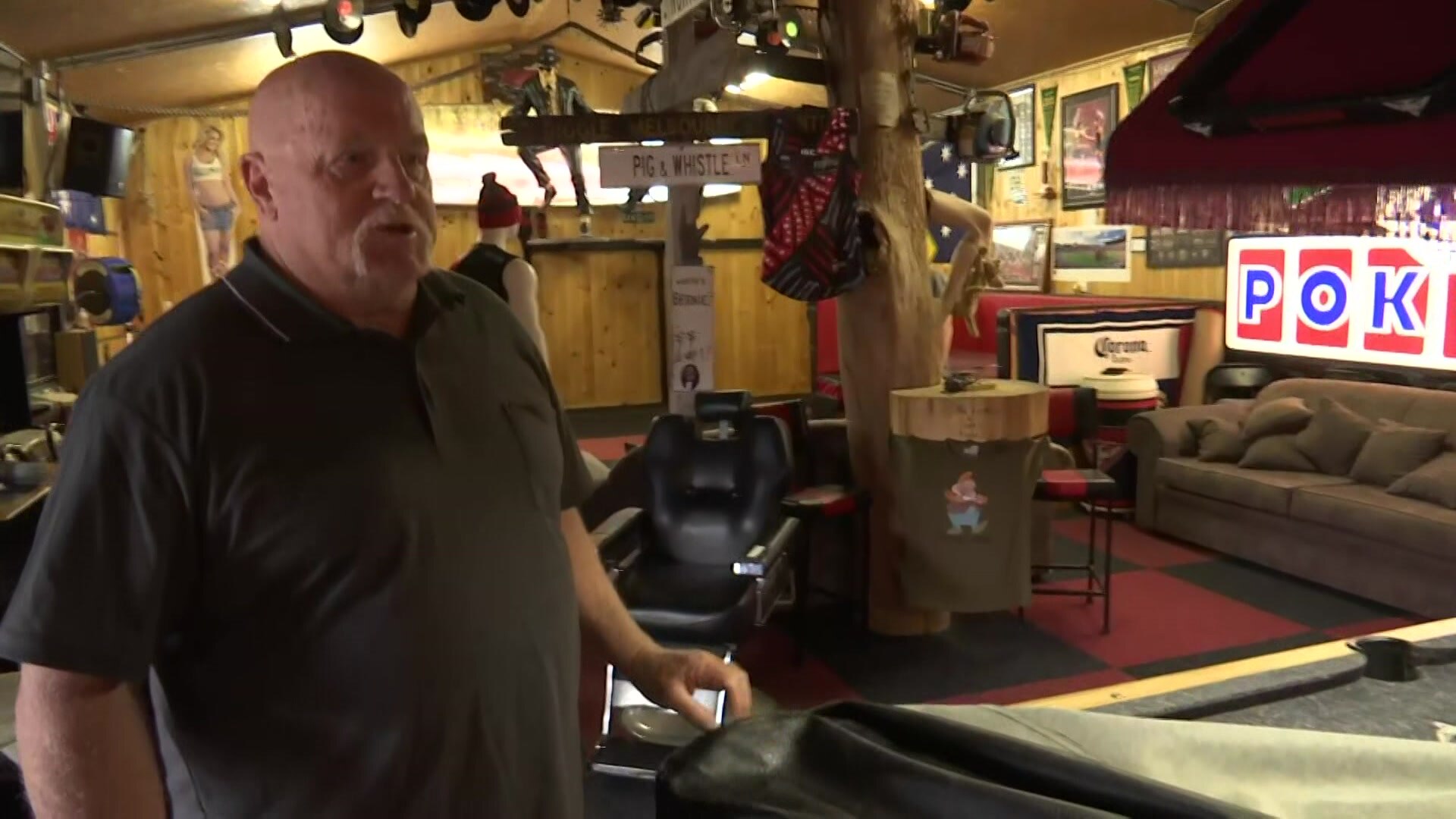 A bald man standing in a room with furniture and a pool table.