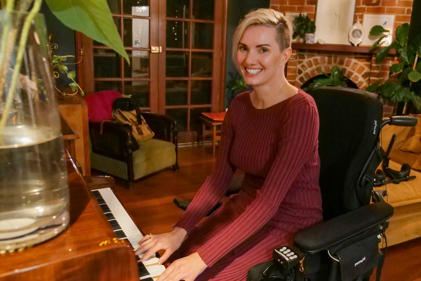 A woman in a burgundy dress, sitting in a wheelchair, playing the piano