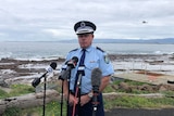 A police officer speaks to the media in a car park overlooking the ocean.
