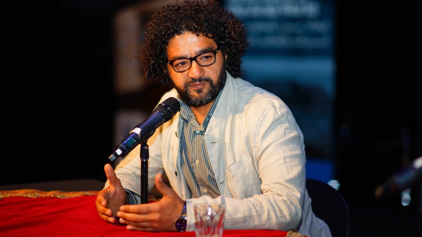 Filmmaker Mohamed Al-Daradji sitting in front of microphone, talking.