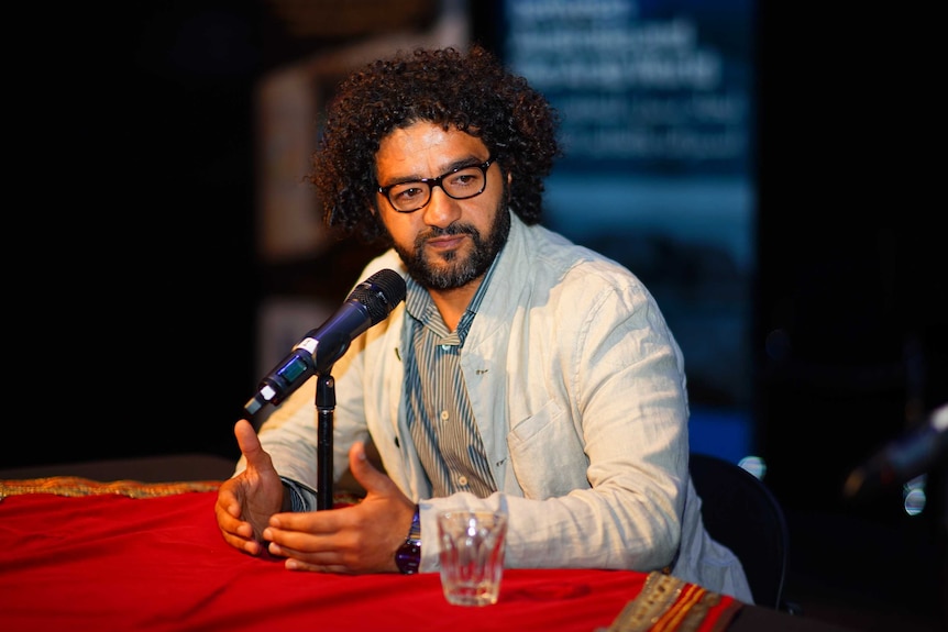 Filmmaker Mohamed Al-Daradji sitting in front of microphone, talking.