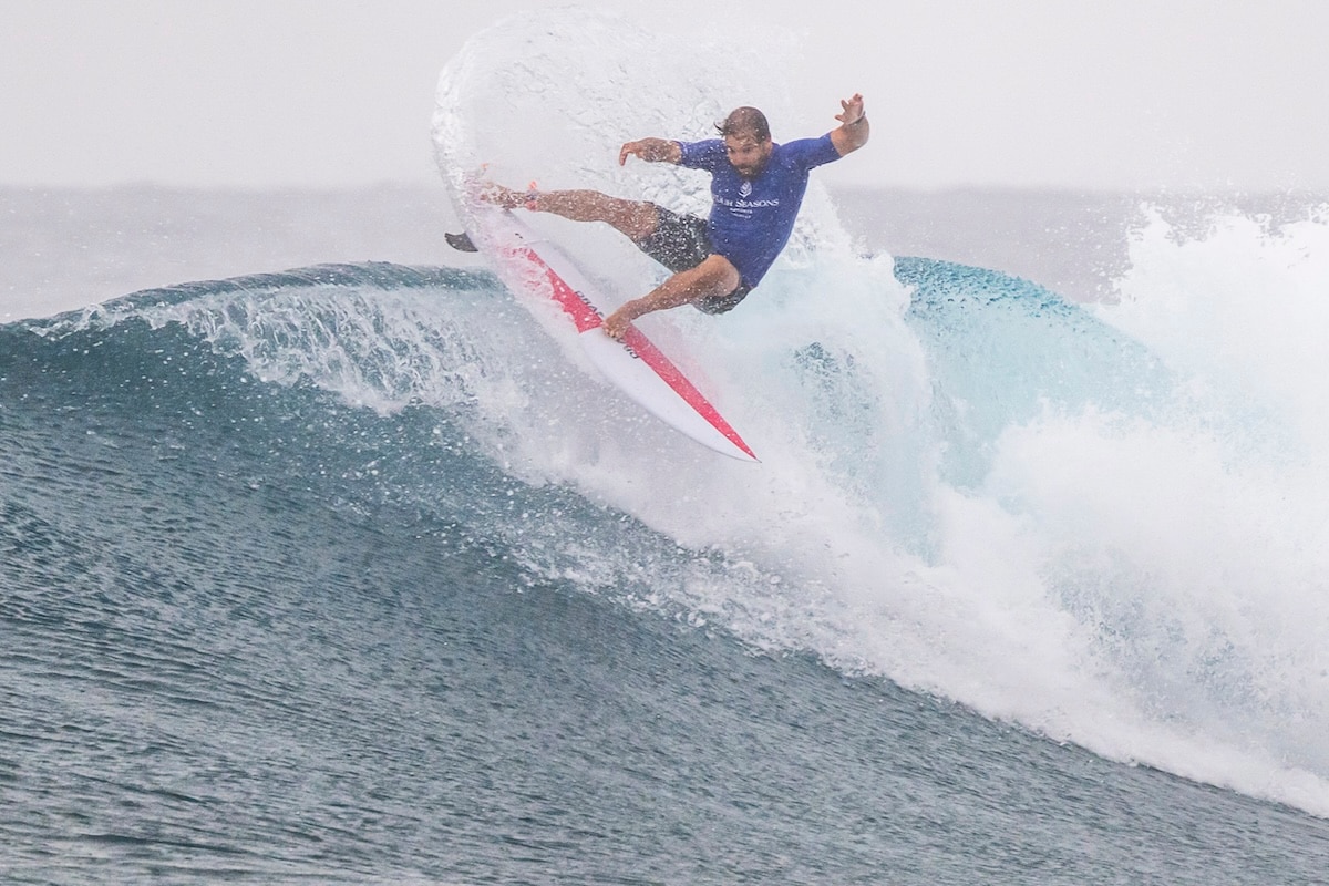 surfer surfing a wave with a blue rashy and white and pink board