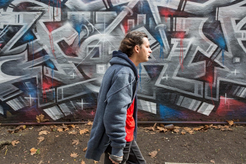 Carpenter walks past a wall of graffiti.