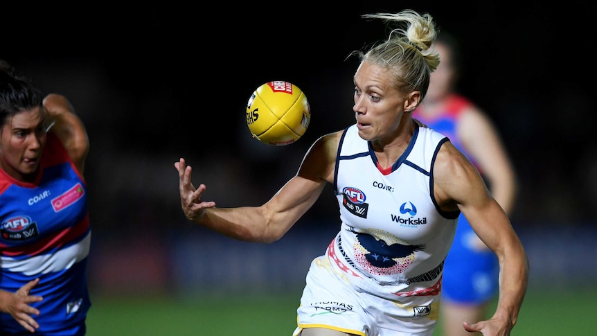An AFLW player reaches out to control the football as she readies herself to run clear.