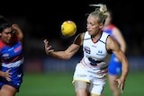 An AFLW player reaches out to control the football as she readies herself to run clear.