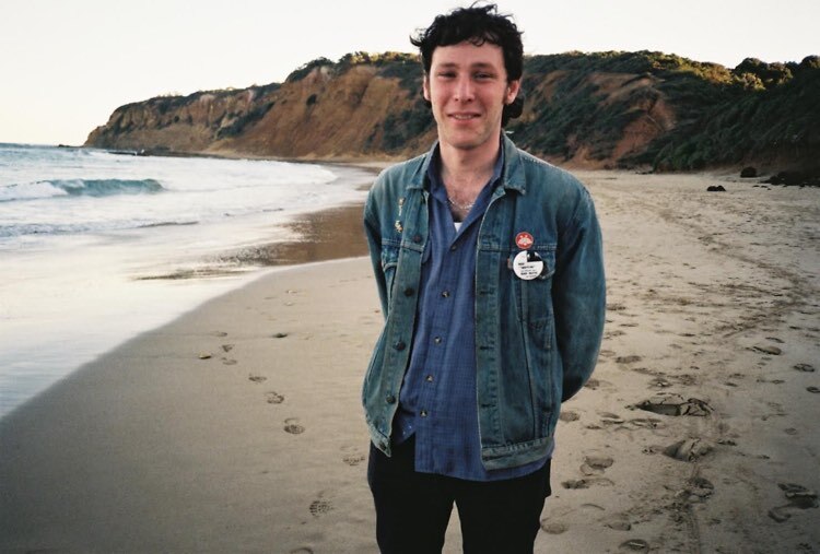 Well-dressed man at the beach smiles at camera.